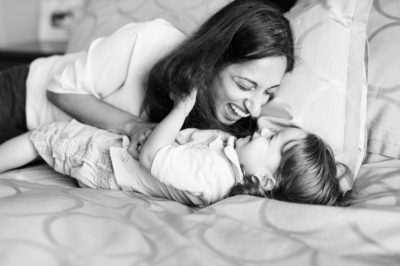 mother tickling laughing child on bed
